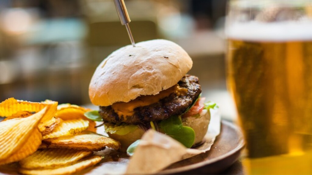 Cheeseburger with lettuce and tomato served alongside crinkle-cut potato chips and a glass of beer.