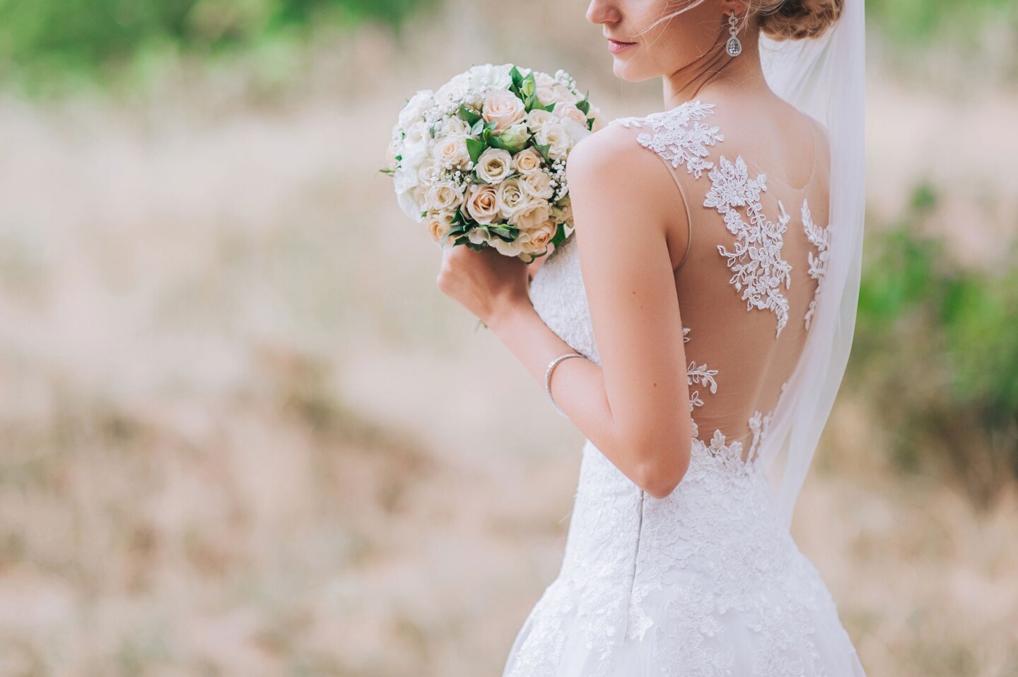 Bride holding a bouquet of white roses in a lace wedding dress at an outdoor wedding setting.