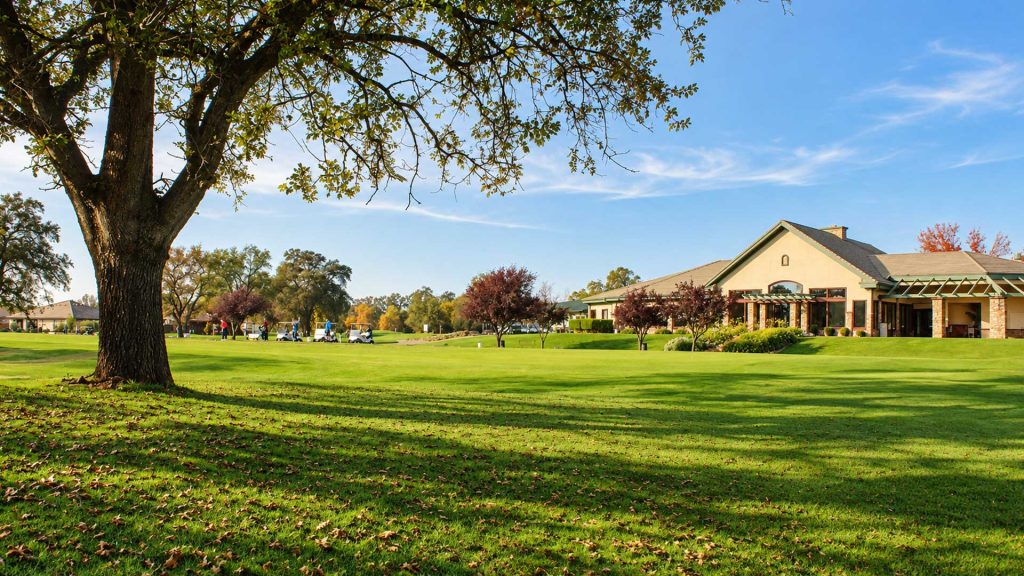 Castle Oaks Golf Club clubhouse and adjacent practice area surrounded by green lawns and mature oak trees in Ione, CA.