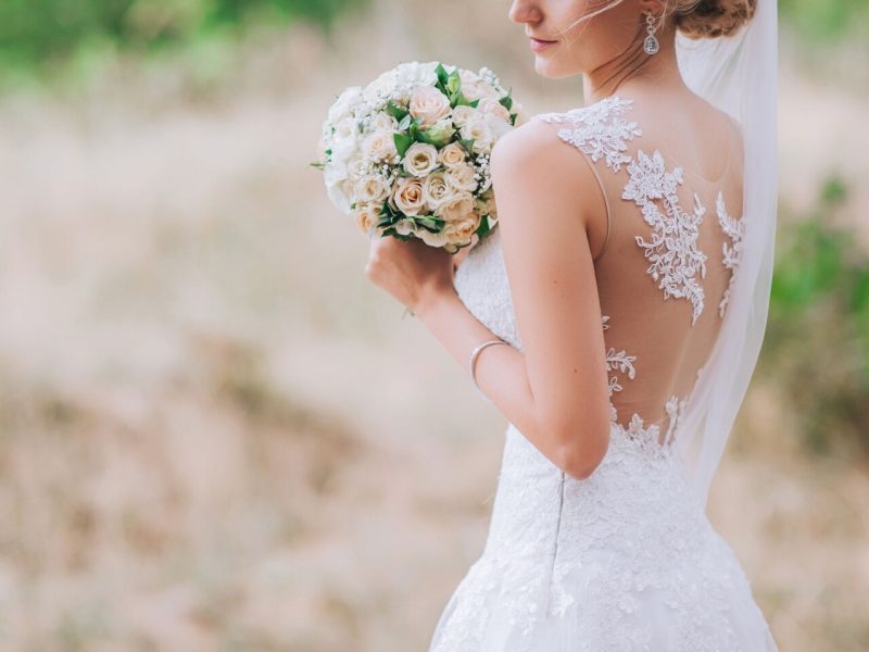 Bride holding a bouquet of white roses in a lace wedding dress at an outdoor wedding setting.