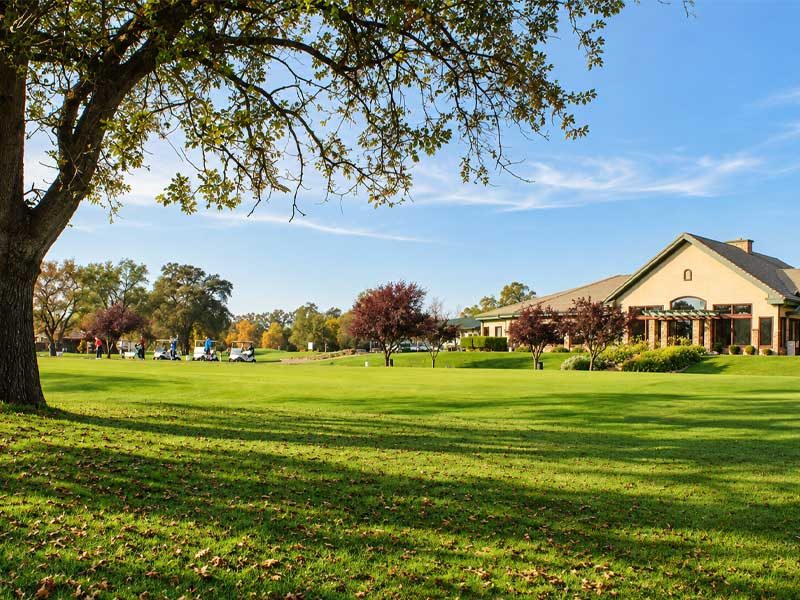 Castle Oaks Golf Club clubhouse overlooking expansive green lawns, mature oak trees, and the golf practice area in Ione, CA.