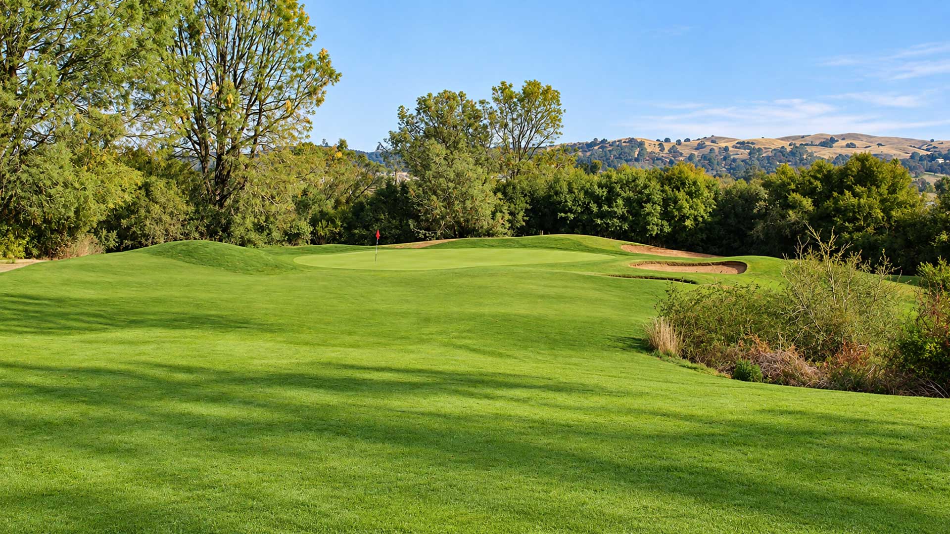 Scenic golf green with a red flag, sand bunkers, and rolling foothills at Castle Oaks Golf Club in Ione, CA.