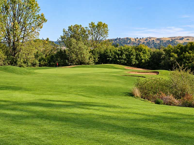 Scenic golf green with a red flag, sand bunkers, and rolling foothills at Castle Oaks Golf Club in Ione, CA.